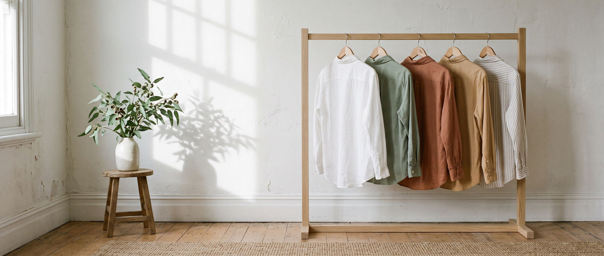 Shirts in warm neutral colours on a wooden clothes rail in a bright room